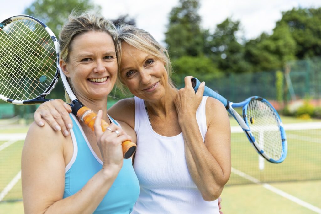 Portrait of two happy mature women on grass court at tennis club